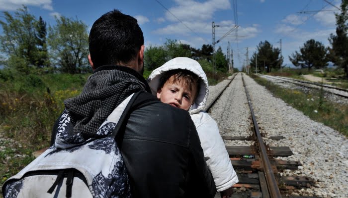 A migrant carries his child as he walks on a railway line at the border post of Idomeni, some 600 km North of Athens, on the border Greece-Macedonia on April 21, 2015. Since Greece bolstered controls along its land border with Turkey along the Evros River, illegal immigrants have turned to the maritime route between Turkey and the Greek islands in the Aegean Sea, notably Lesvos, Samos, Kos and Chios. 2015 started with a major increase in the number of Aegean crossings : 10,445 against 2,863 in the same period of 2014, according to the Greek port police. AFP PHOTO / SAKIS MITROLIDIS / AFP PHOTO / SAKIS MITROLIDIS